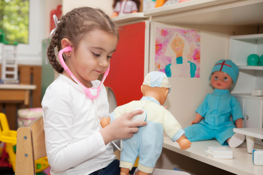Little girl playing doctor with a doll in the nursery