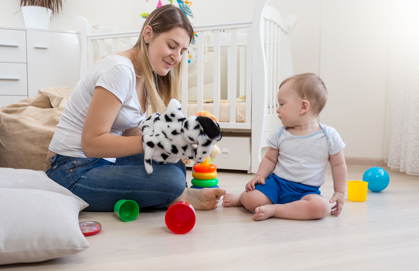 Beautiful smiling mother wearing dog puppet on hand and playing with her baby boy