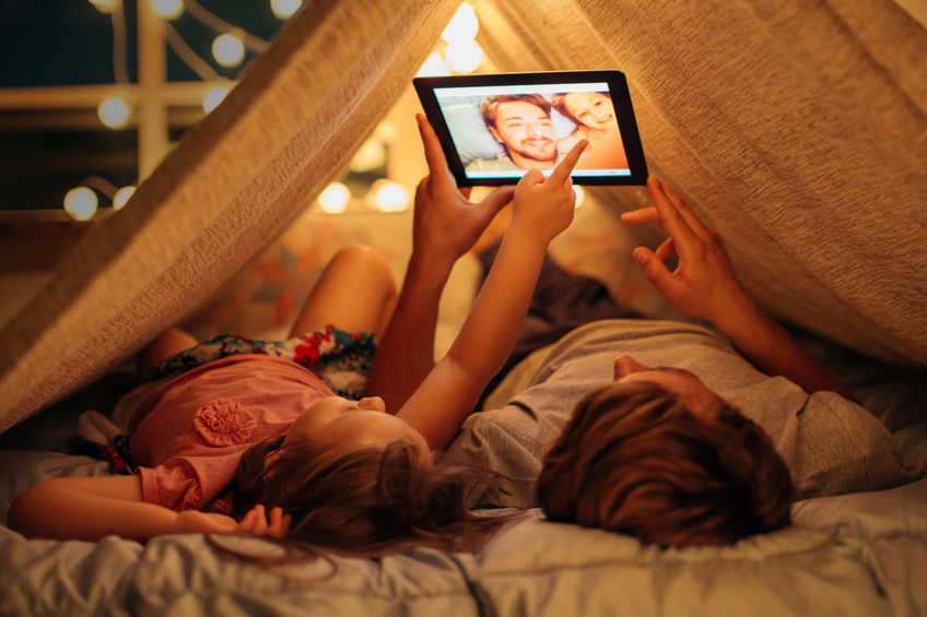 Father and daughter enjoying at home. Lying on bed at night in do it yourself tent and using digital tablet together. Taking selfies and watching photos.